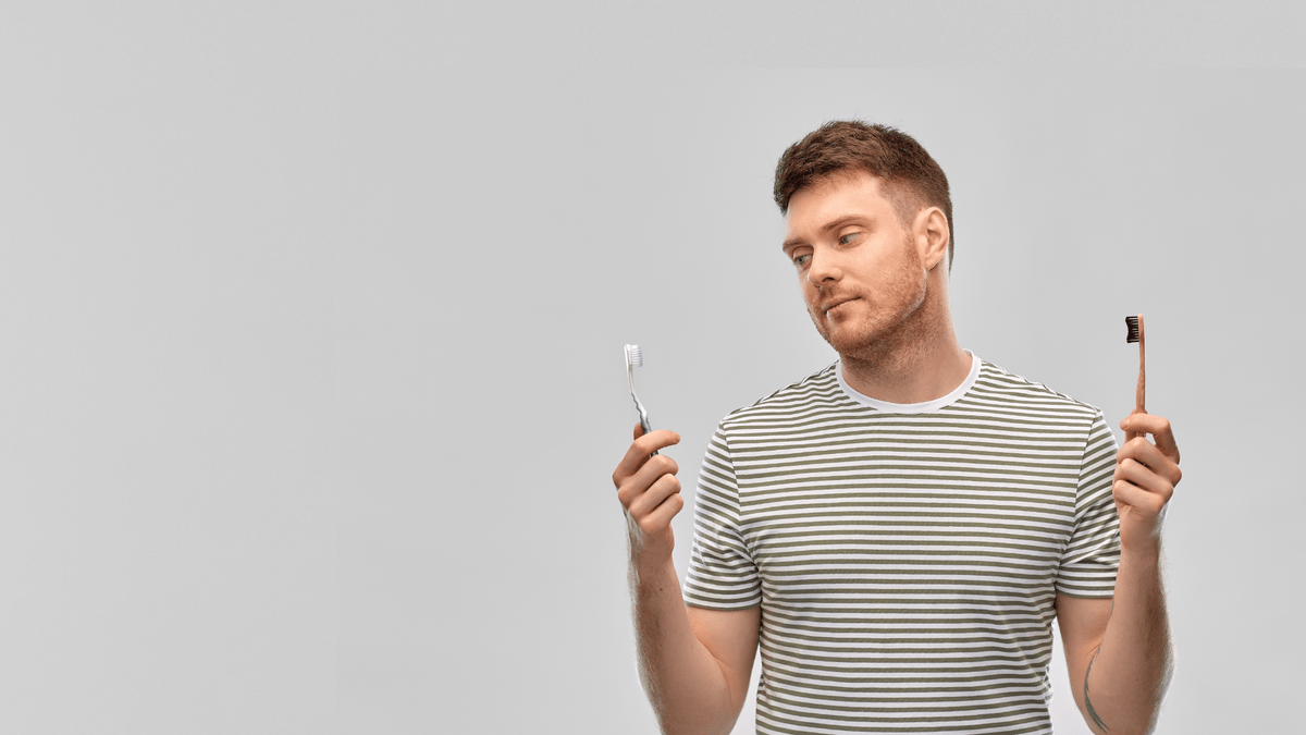A man comparing bamboo toothbrush with plastic toothbrush